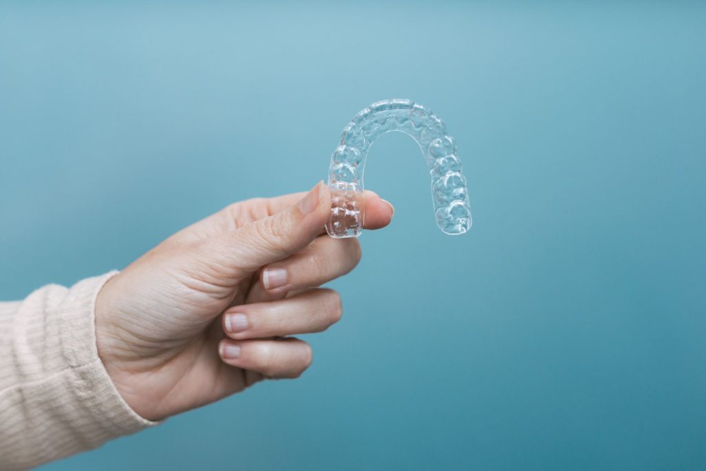 A hand holding a clear, removable aligner tray against a teal background